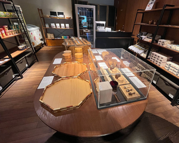 ラフォーレ箱根強羅 湯の棲のスーベニアショップでの「手神」ブランドの木製品が並ぶ展示台。寄木縁八角盆、寄木芯八角茶筒、ガラスケース内のも小物が美しくディスプレイされている。