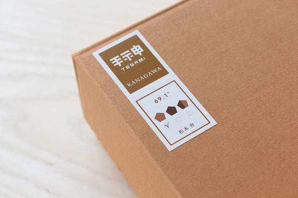 手神ブランドの切手モチーフタグ - 69.1°の商品表示と松本育の作者名が記載された商品ラベル