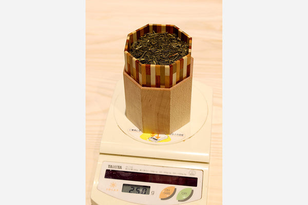 茶葉の量を測る様子。タニタの計量器に乗せられた八角形の木製茶筒に茶葉が入っている。